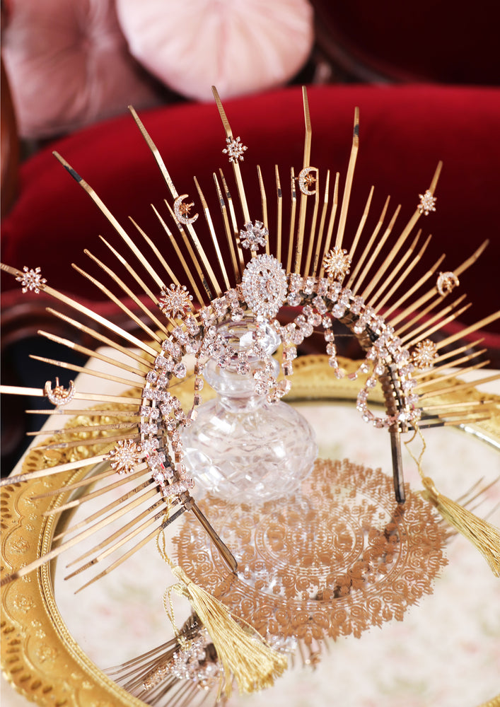 A celestial headpiece is resting on a table. It is gold and silver, encrusted with sparkling rhinestones